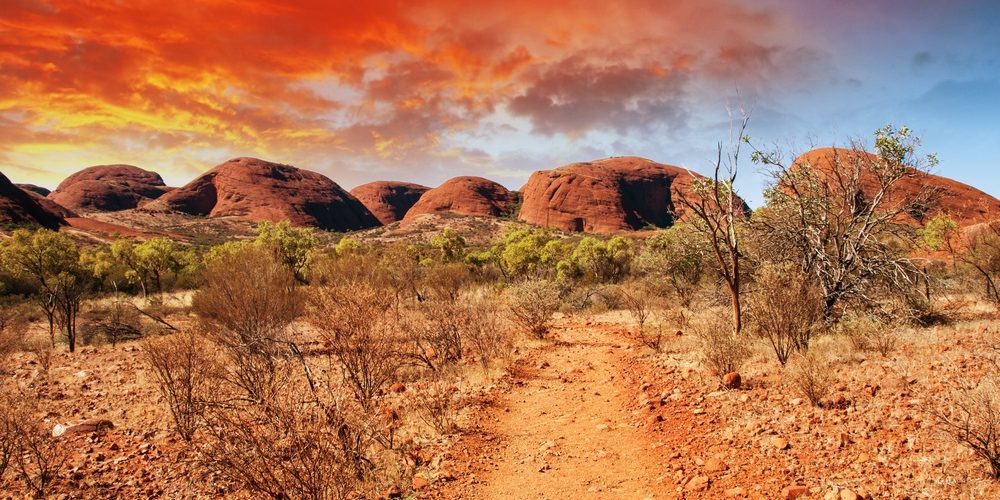 AUS_outback A dirt path leads toward large, red rock formations under an orange and blue sky.
