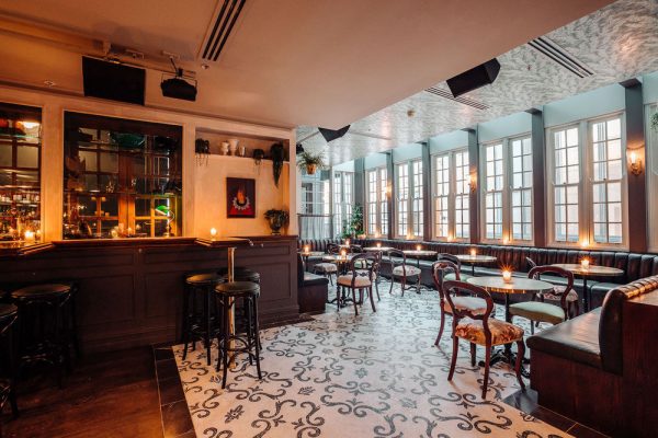 CON+8 The interior of a stylish bar with a tiled floor, comfortable seating, and warm lighting.