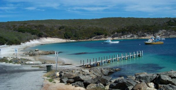 Fishery Beach Boat Harbour A small beach and bay with a wooden pier and two boats anchored in the water.