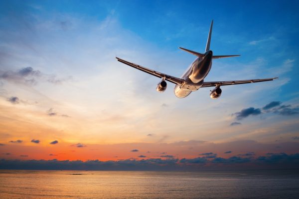A passenger plane flies low over the ocean during a vibrant sunrise or sunset.