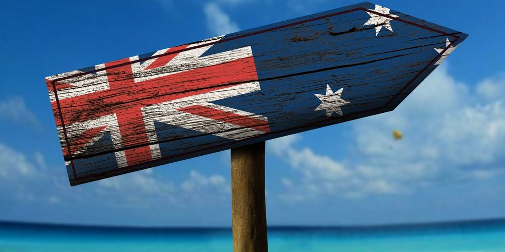 A wooden arrow sign with a weathered Australian flag pointing towards a beach.