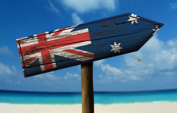 aueflag A wooden arrow sign with a weathered Australian flag pointing towards a beach.