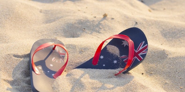 A pair of flip-flops with a design of the Australian flag on a sandy beach.