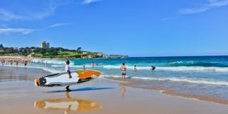 People on a sunny Bondi Beach with a stand-up paddleboard on the sand.