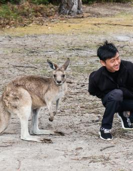 A man smiles while crouching near a kangaroo.
