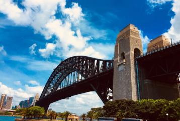 Sydney Harbour Bridge under a bright blue sky with clouds.